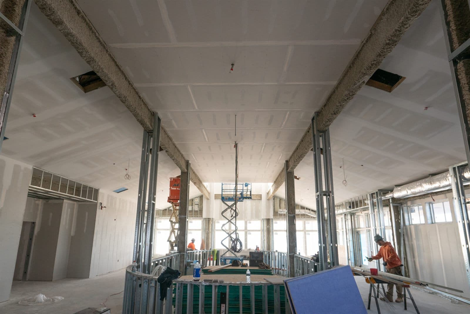 Commercial drywall corridor being finished, with a lift staged for overhead work